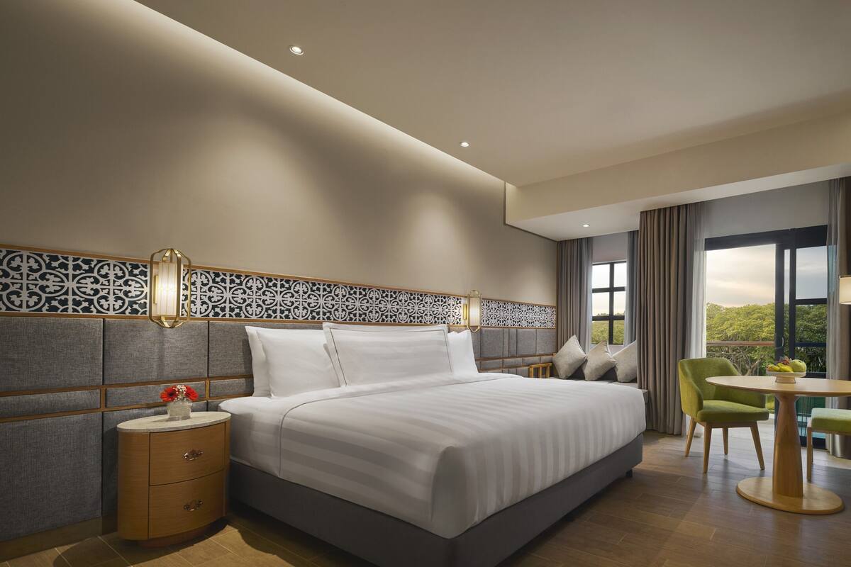 Een moderne hotelkamer met een groot bed, een tafeltje met een stoel, een televisie en uitzicht op groen.
