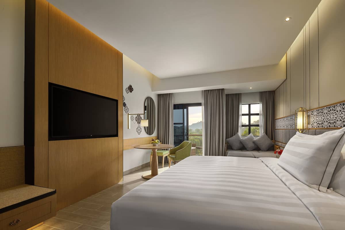 Een moderne hotelkamer met een groot bed, een flatscreen televisie aan de wand, een klein bureau met een stoel en een balkon met uitzicht.