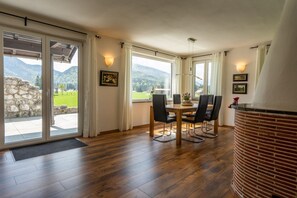 Ein Essbereich mit Tisch und Stühlen, großen Fenstern mit Vorhängen und Blick auf Berge.