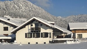 Ein mit Schnee bedecktes Chalet mit Balkon, umgeben von verschneiten Bergen.