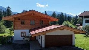 A two-story wooden house with a red-tiled garage and a small porch. - Chalet 125qm für Max. 6 Personen, 3 Sep. Schlafzimmer (Reit im Winkl)