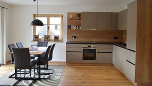 A modern kitchen with a dining area, wooden cabinets, and a built-in oven. - Chalet 125qm für Max. 6 Personen, 3 Sep. Schlafzimmer (Reit im Winkl)
