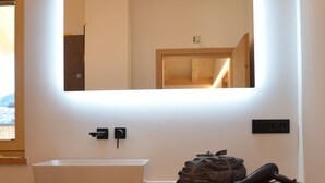A bathroom with a wooden vanity, a white sink, a mirror with integrated lighting, and a towel rack. - Chalet 125qm für Max. 6 Personen, 3 Sep. Schlafzimmer (Reit im Winkl)