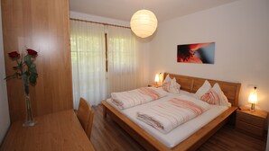 Een netjes ingerichte slaapkamer met een houten bed, bedlampen, een eettafel met stoelen, en een vaas met bloemen.
