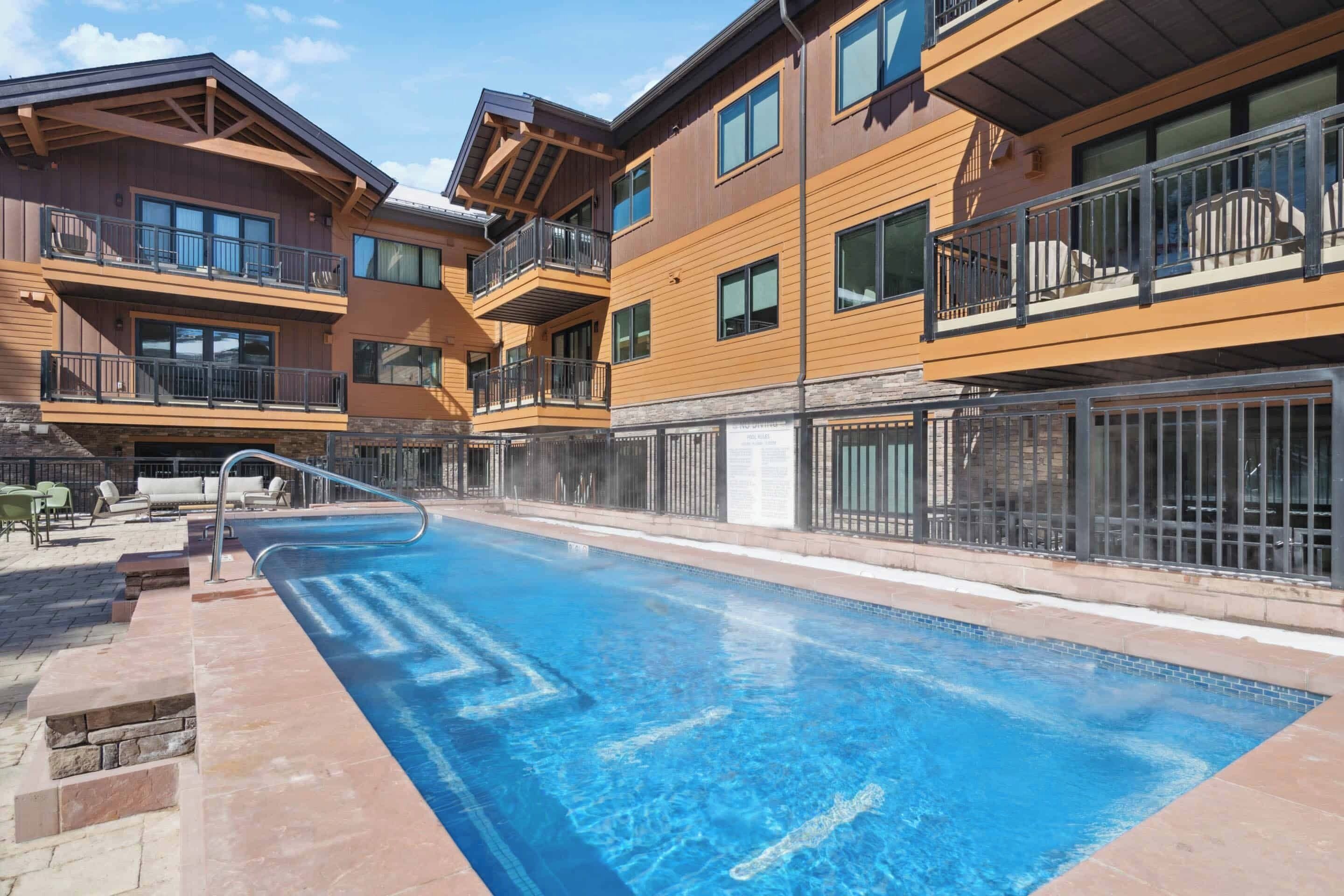 A modern hotel with a swimming pool, outdoor seating, and balconies.