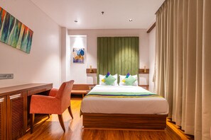 A hotel room with a wooden bed, a desk, a chair, and a painting on the wall.