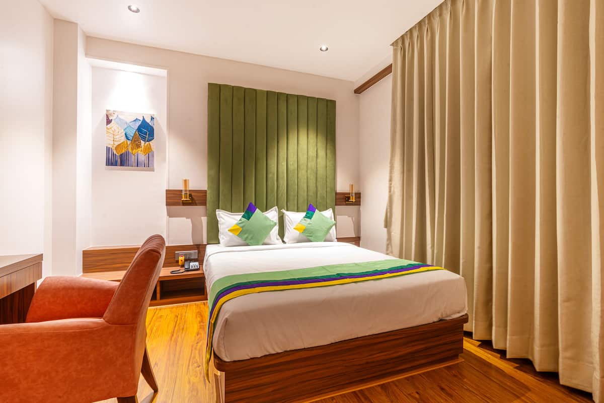 A hotel room with a bed, a chair, a nightstand, a painting, and curtains.