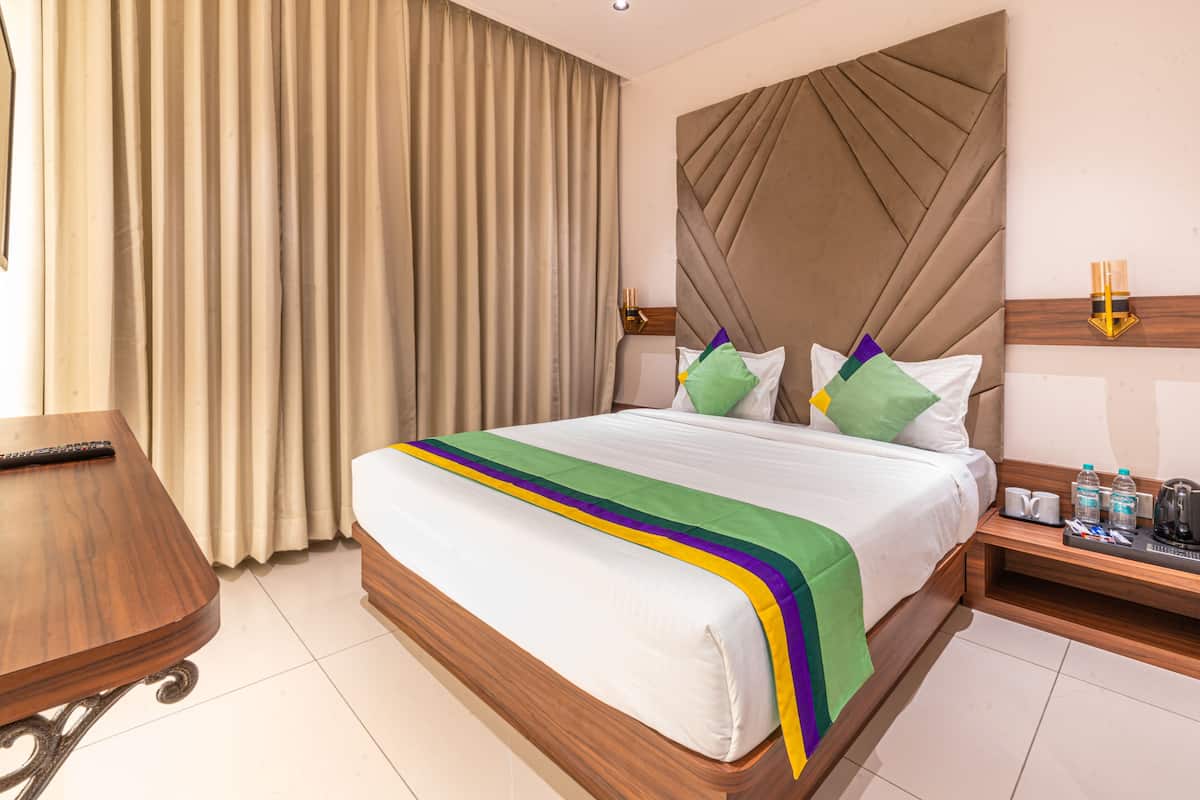 A hotel room with a large bed, a wooden nightstand, a desk, and a chair.