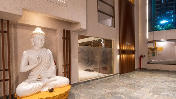 A large Buddha statue in a meditative pose on a golden pedestal, set against a modern building facade with large windows and a patterned floor. - Treebo Premium Heritage Grand, Thane (Thane)