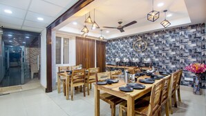 A dining area with wooden tables and chairs, a ceiling fan, and pendant lights. - Treebo Fortune Home Expressway (Noida)