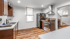 Eine moderne Küche mit Edelstahl-Kühlschrank, Backofen und Herd, Holzboden und weißen Schränken.