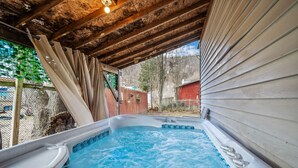 Ein Whirlpool unter einem Holzdach mit Blick auf einen eingezäunten Garten und Bäume.