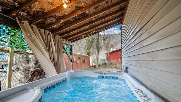 Ein Whirlpool unter einem Holzdach mit Blick auf einen eingezäunten Garten und Bäume.