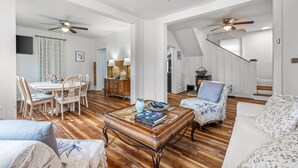 Ein geräumiges Wohnzimmer mit Holzboden, einer Essecke mit Tisch und Stühlen, einem Sofa und einem Deckenventilator.