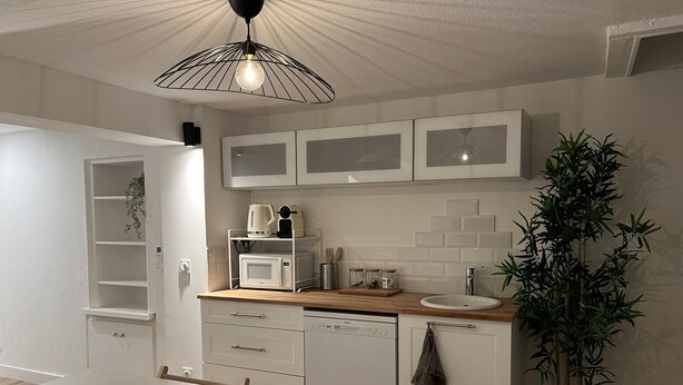 Eine moderne Küche mit weißen Schränken, einer Holz Arbeitsplatte, einem Spülbecken, einem Geschirrspüler und einer Pendelleuchte.