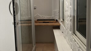Ein schmaler Flur mit Glastür, einer hölzernen Bank und einem Fenster.