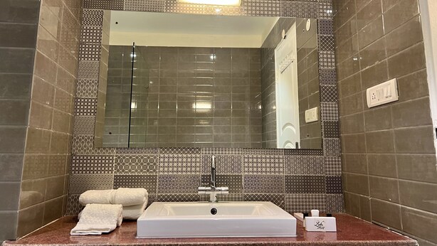 Une salle de bain avec des carreaux décorés, un grand miroir, un lavabo et un porte-serviettes.