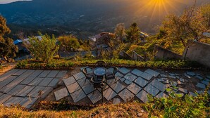 Une terrasse avec une table et des chaises, offrant une vue sur un paysage montagneux au coucher du soleil.