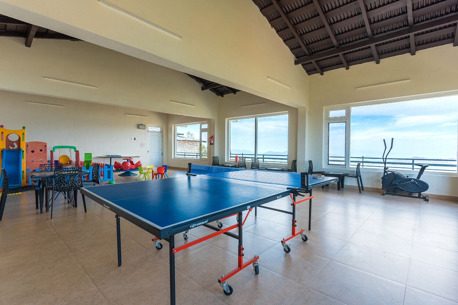 A spacious indoor area with ping pong tables, exercise bikes, and colorful play equipment.