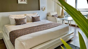 Een moderne hotelkamer met een groot bed, een klein tafeltje en een stoel. Er is een raam met gordijnen en uitzicht op buiten.
