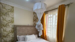 Un lit bien fait, recouvert d’une couverture blanche et jaune, avec un baldaquin et une serviette enroulée posée sur le lit.