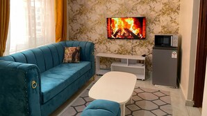 Un salon avec un canapé bleu, une table basse blanche, un téléviseur à écran plat, un four à micro-ondes et un réfrigérateur.