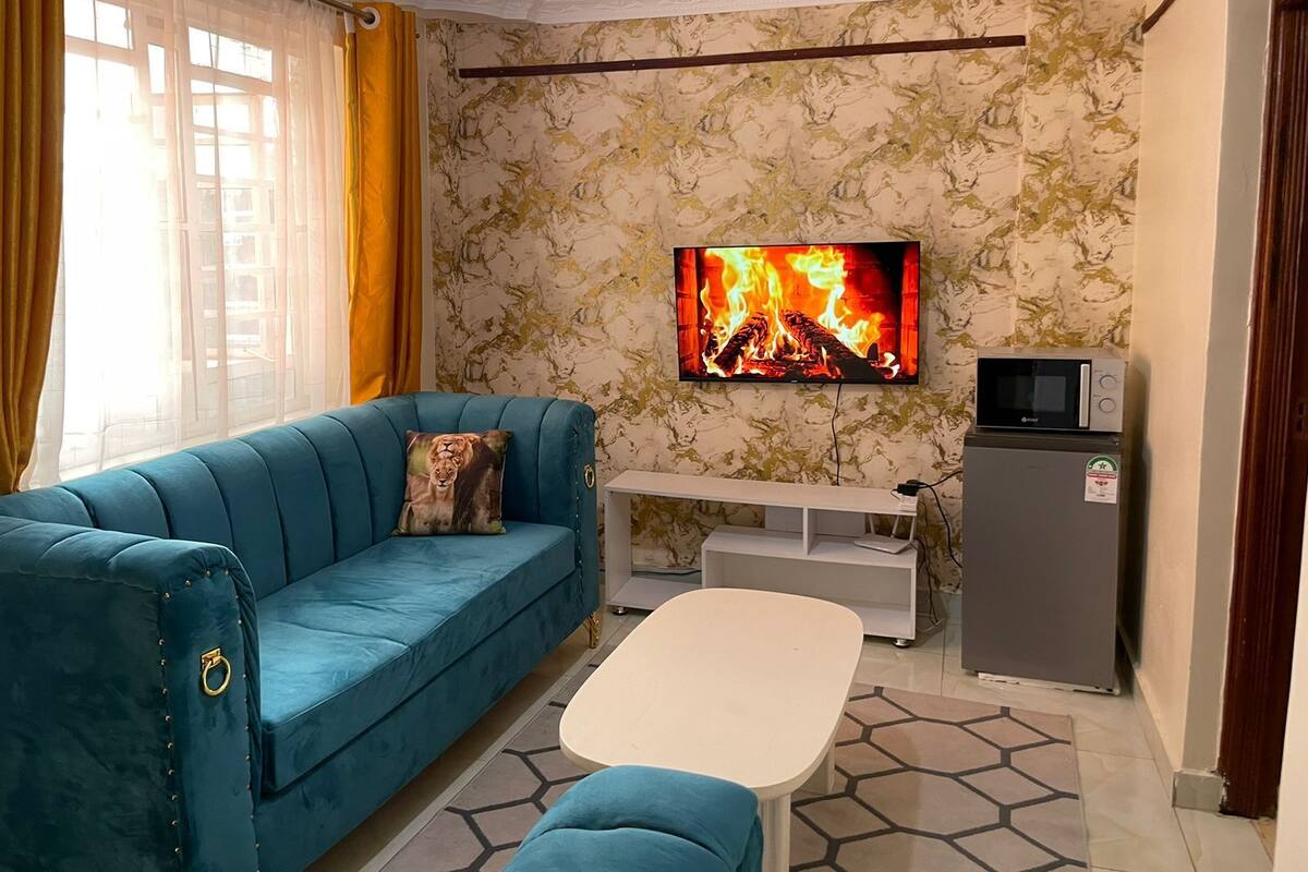 A living room with a blue sofa, a white coffee table, a flat-screen TV, a microwave, and a refrigerator.