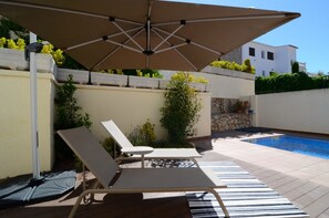 Ein Poolbereich mit Liegestühlen, einem großen Sonnenschirm und einer Steinmauer.
