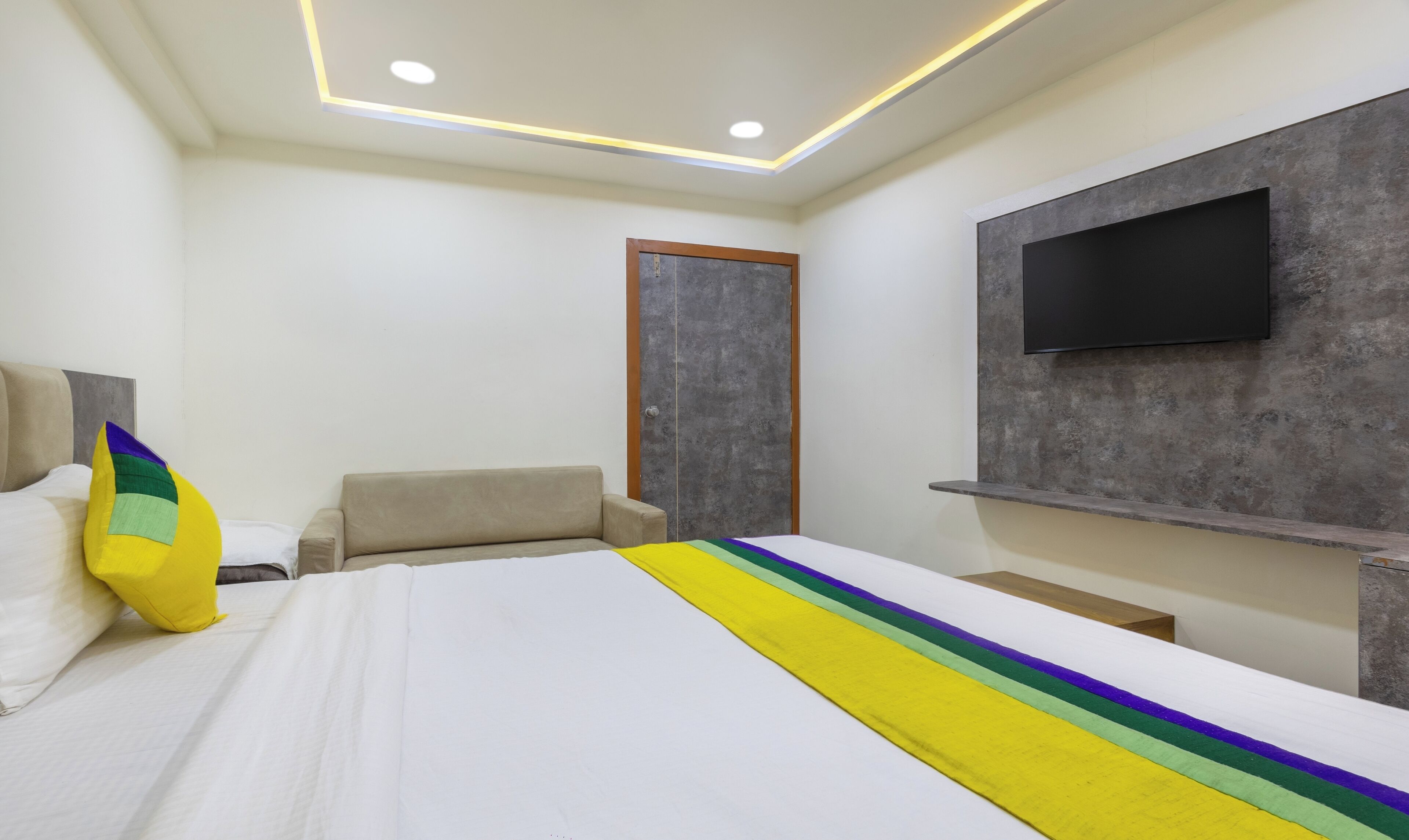 Una camera d'albergo con un letto, una sedia, una TV a parete e una porta.