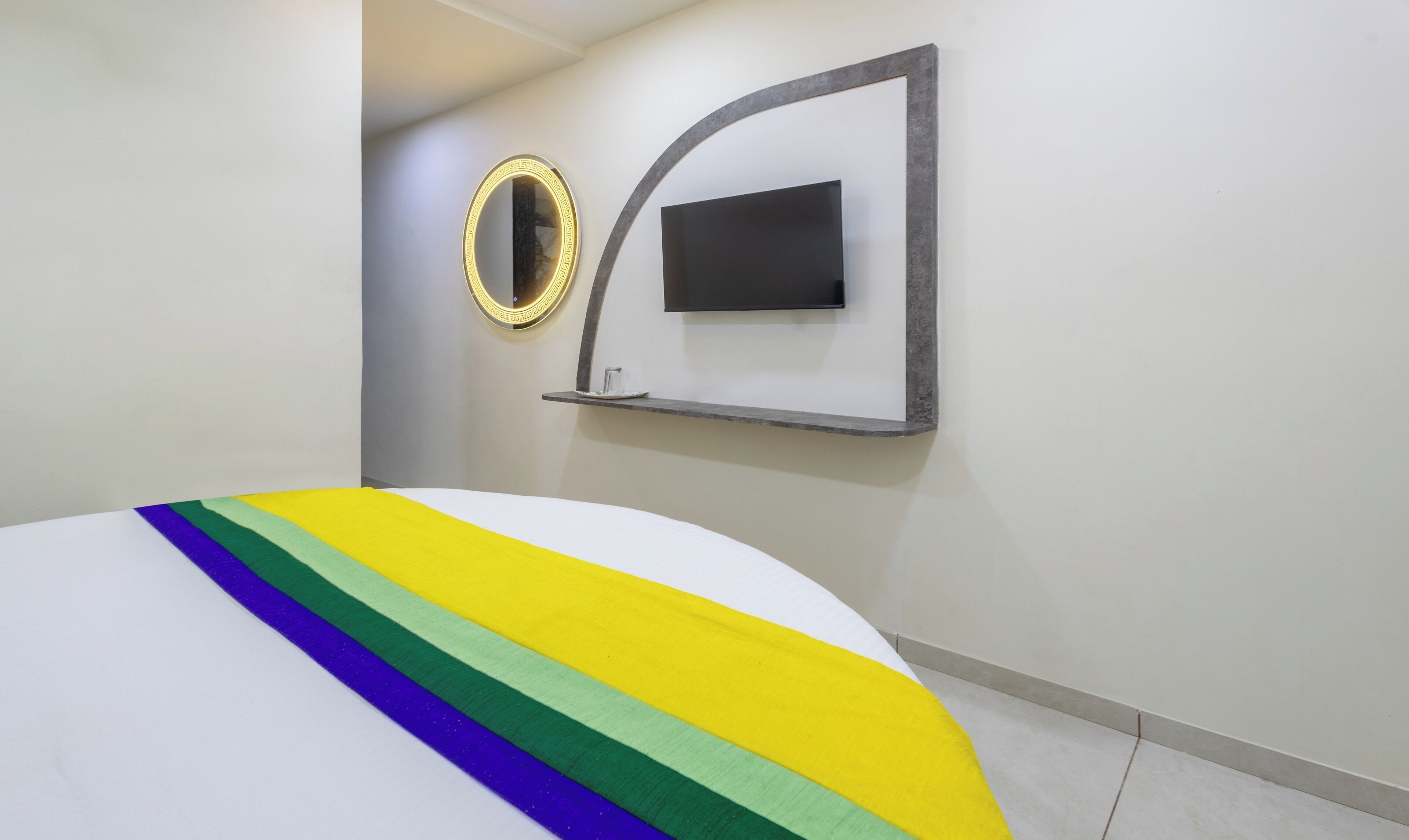 A modern hotel room with a bed, a wall-mounted TV, and a decorative mirror.