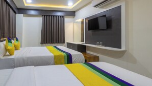 A hotel room with two beds, a flat-screen TV mounted on the wall, a small wooden side table, and a window with curtains. - Itsy Hotels Signature, Nehru Nagar (Ahmedabad)