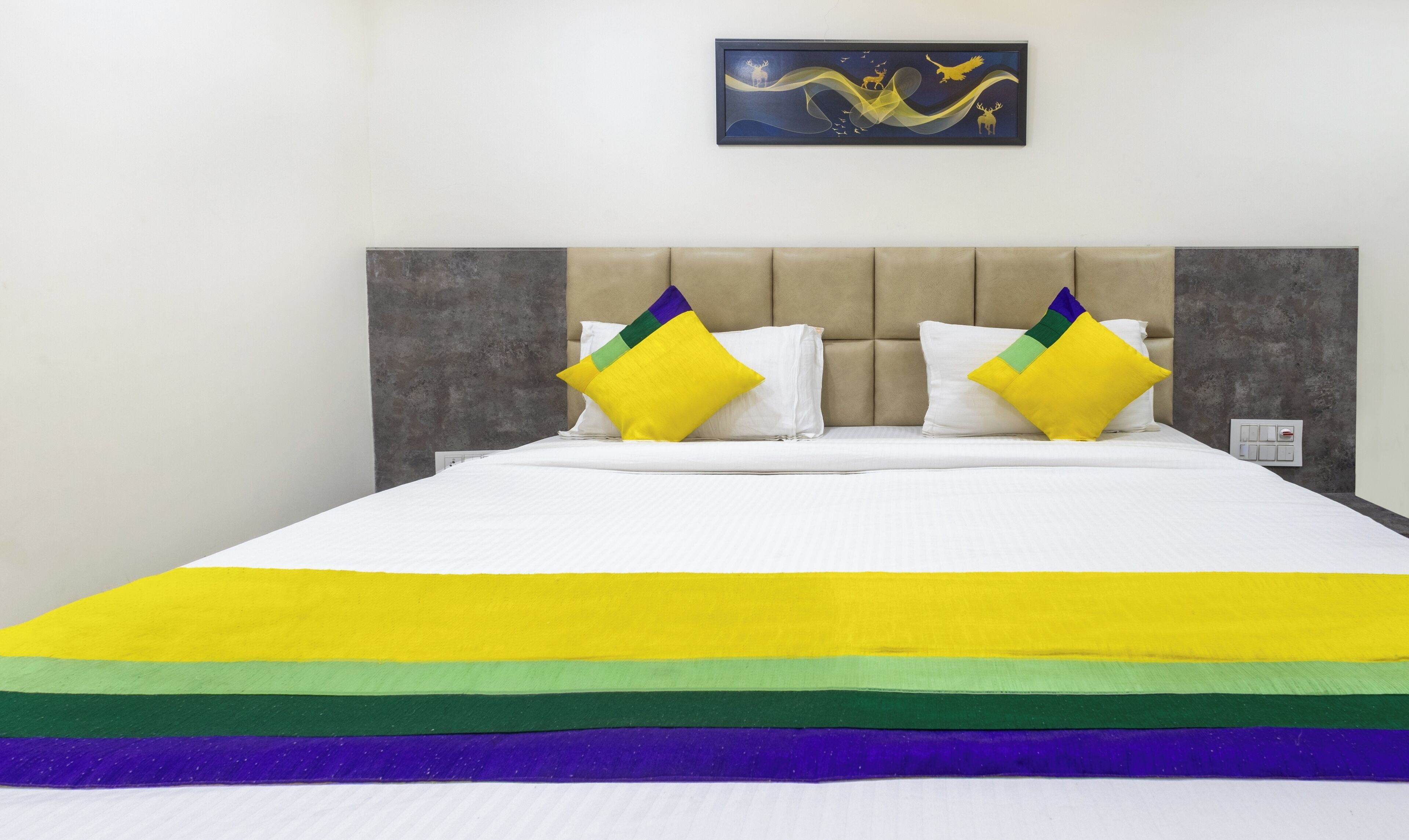 Un lit avec un matelas blanc, deux oreillers et une couverture colorée.