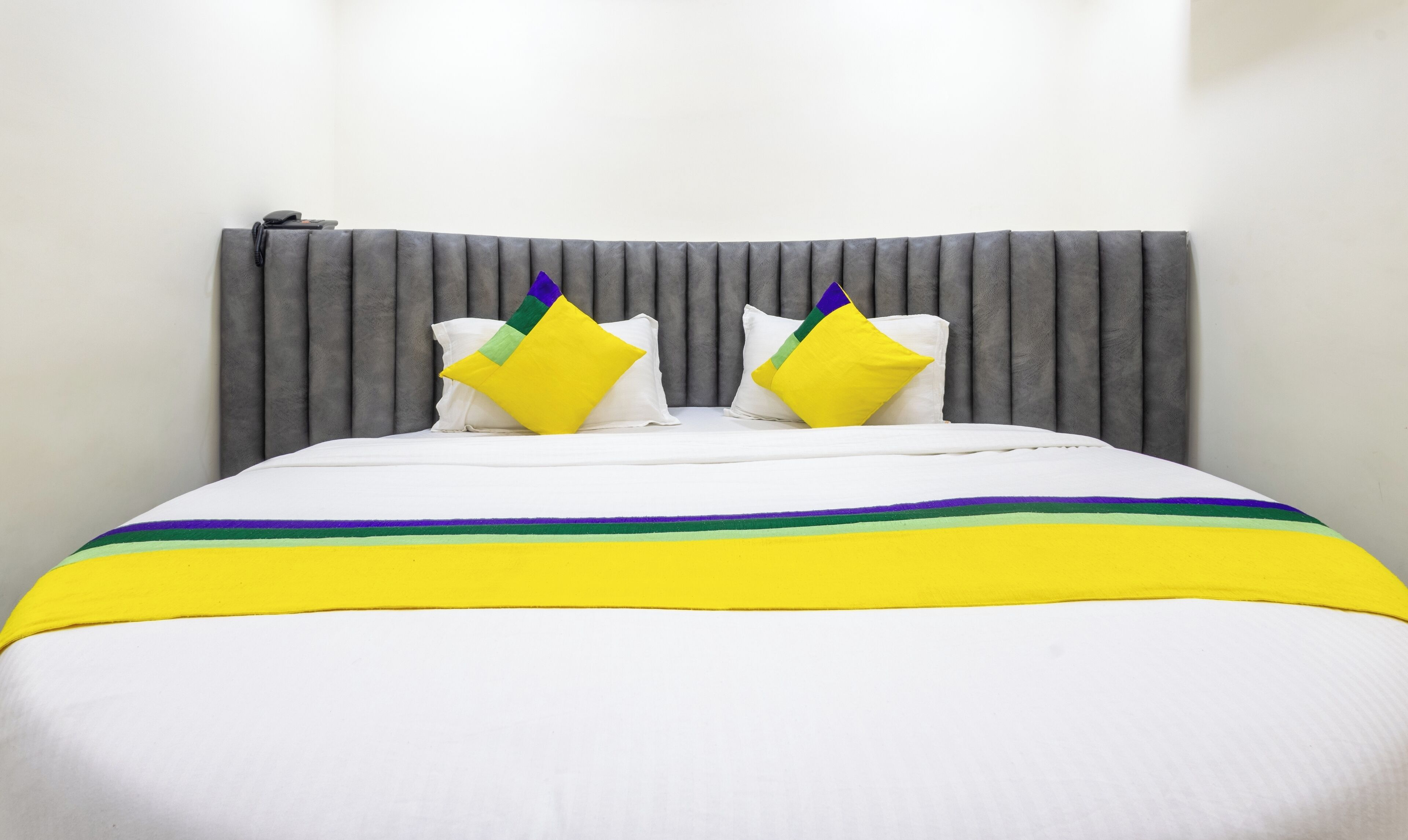 A bed with a grey upholstered headboard, white bedding, and two pillows with a yellow and green design.