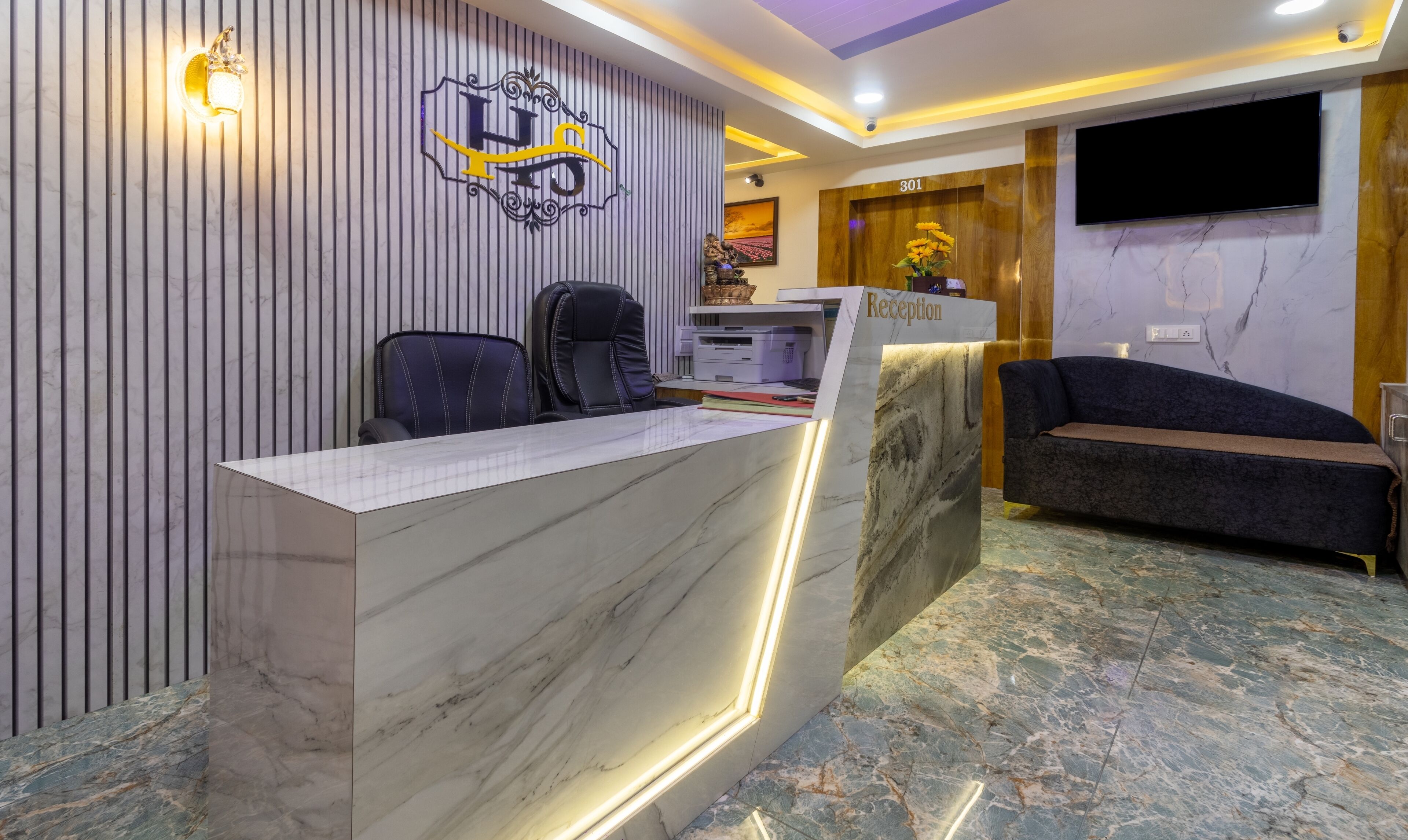 A reception area with a marble reception desk, a reception sign, a flat-screen TV, and a sofa.