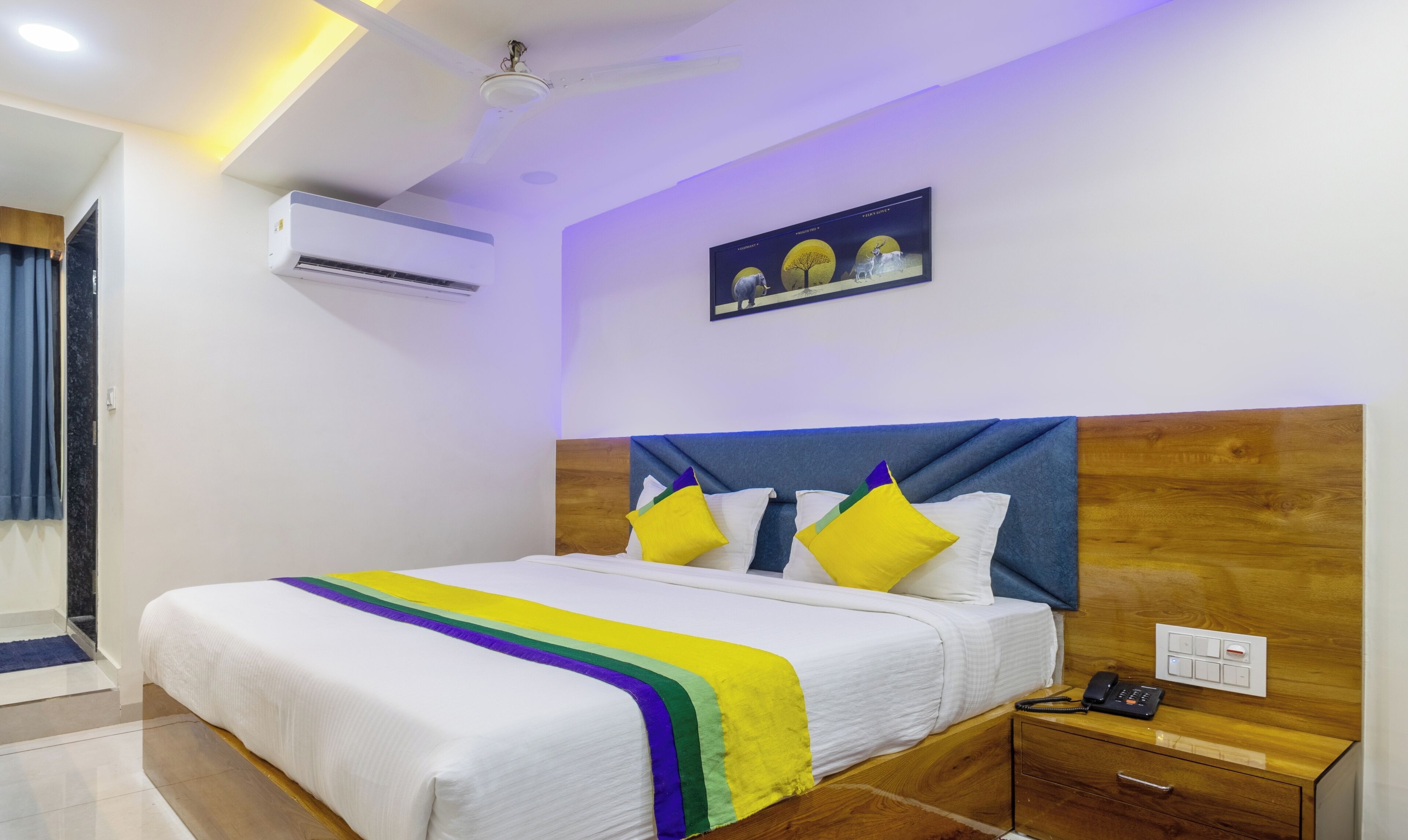 A hotel room with a bed, bedside table, and a wall-mounted air conditioner.