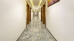 A long, narrow hallway with marble flooring and wooden doors on both sides. - Itsy Hotels Signature, Nehru Nagar (Ahmedabad)