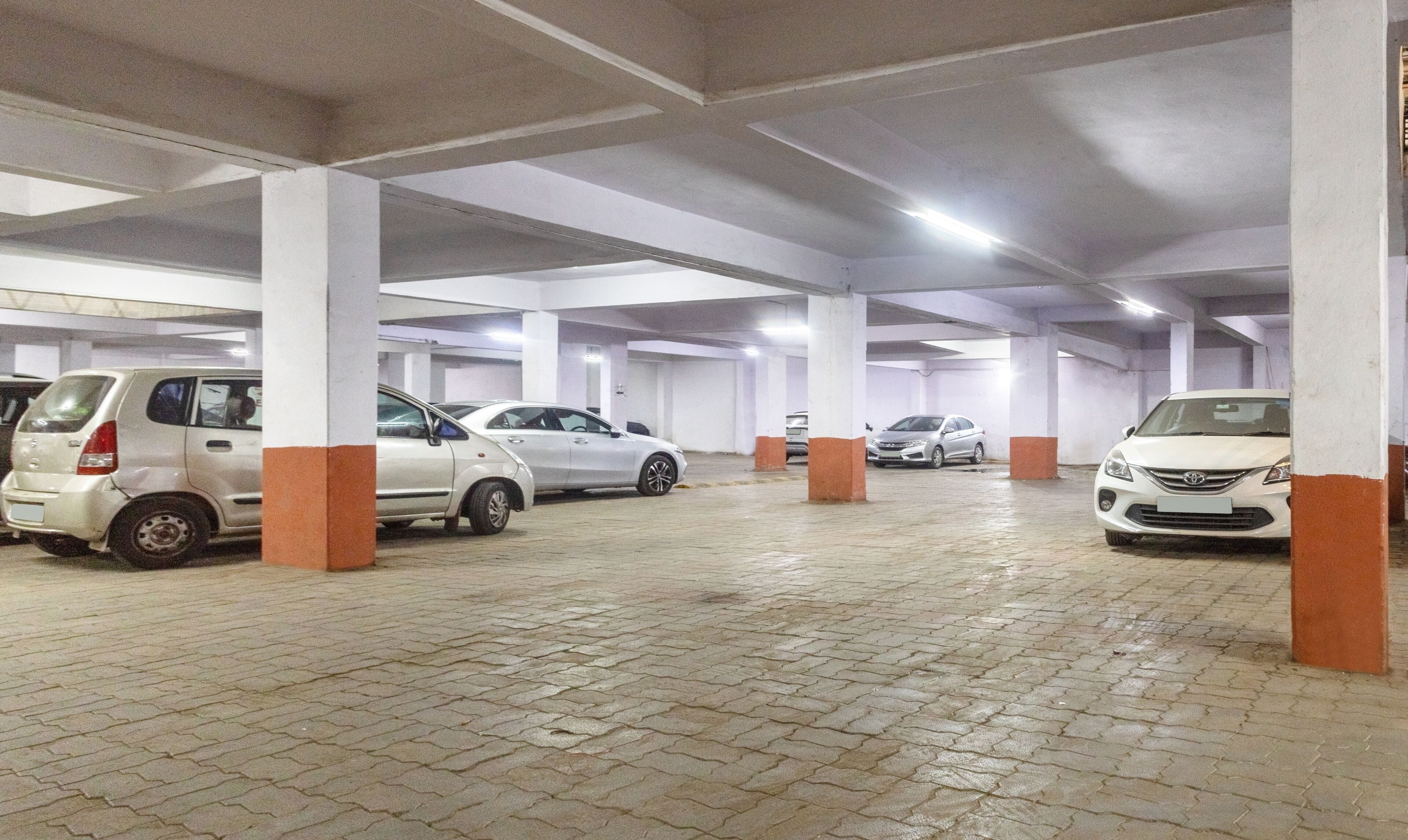 Un parking où de nombreuses voitures sont garées sous des piliers blancs et orange.