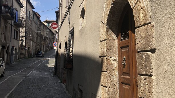 A narrow cobblestone street with historic buildings, a wooden door with a metal handle, and a stop sign. - Pergi Palace (Tolfa)