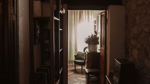 A narrow hallway with a rustic ceiling, a wooden door on the left, and a chair and table in the center. - Pergi Palace (Tolfa)