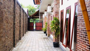A narrow brick corridor with tiled flooring, potted plants, and a wooden gate. - Vamana Bangsal (Pemenang)
