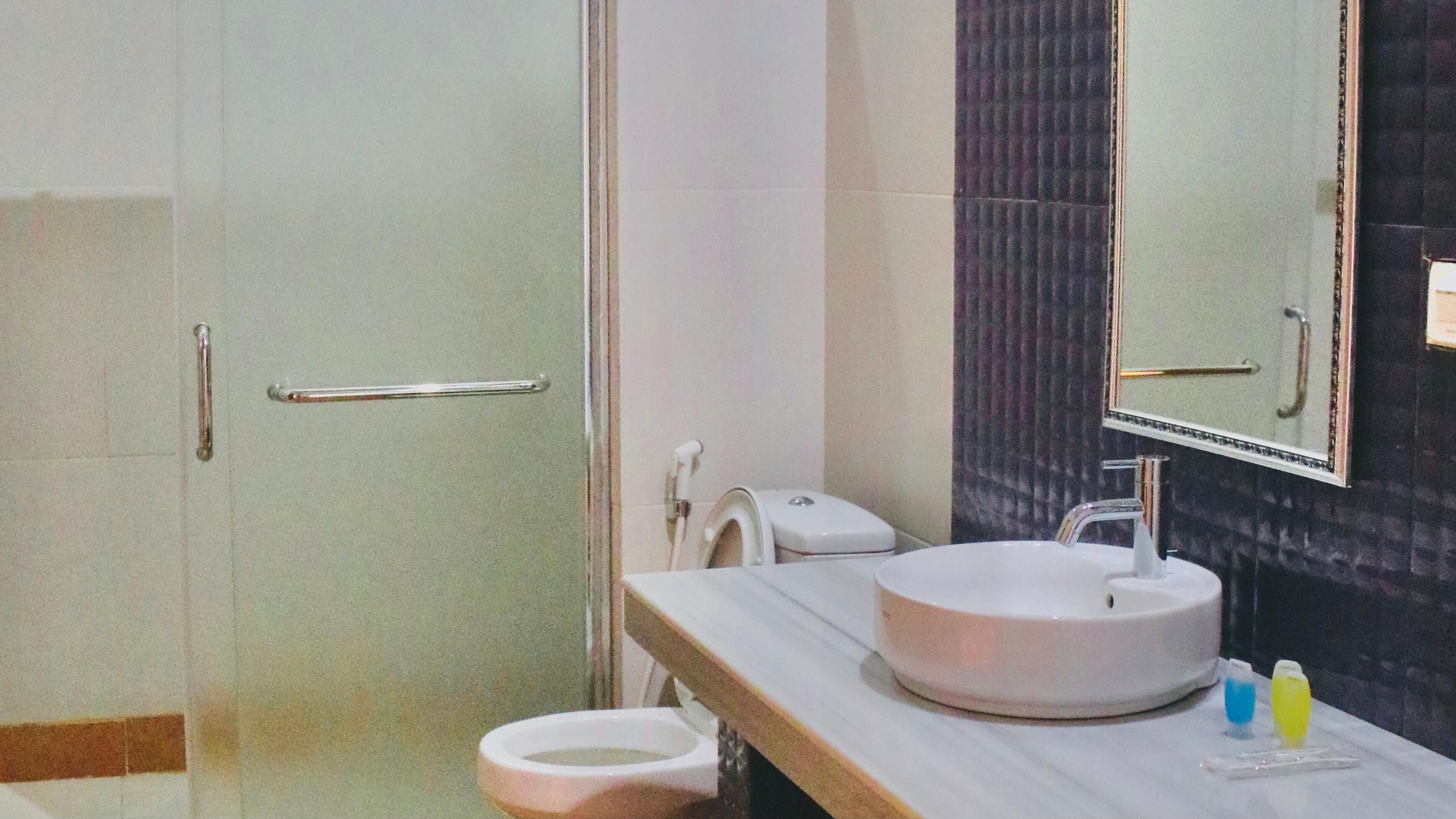 A modern bathroom with a white sink, a handheld showerhead, and a toilet.