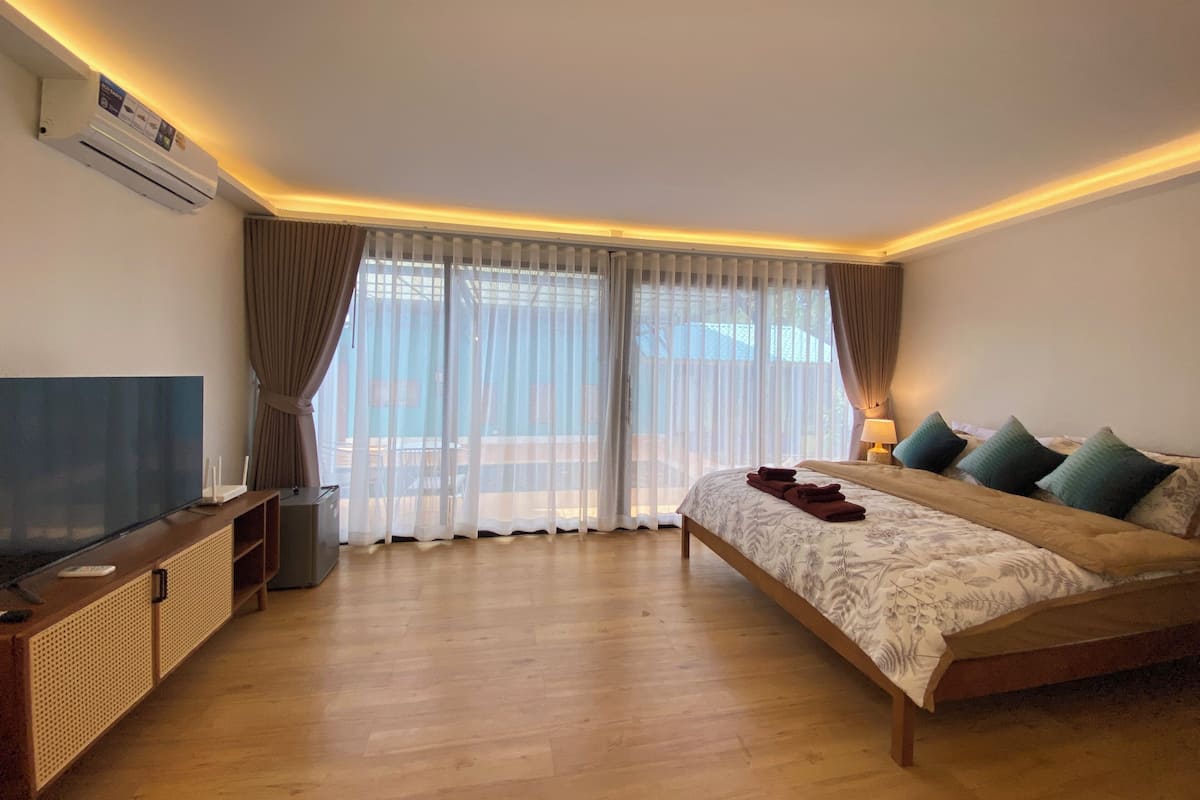 A bedroom with a large bed, a TV, and a wooden floor.