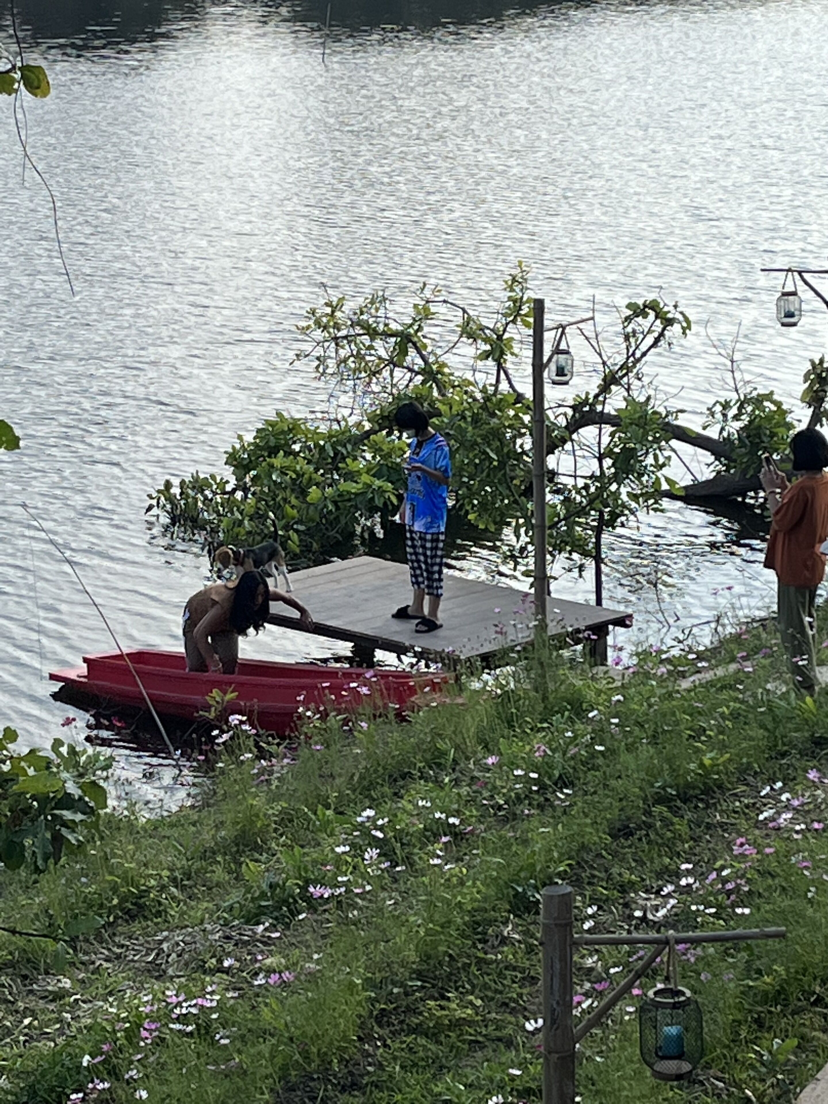 A dock with a wooden platform, a red boat, and a person standing on the platform.
