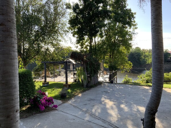 A gazebo with outdoor seating, surrounded by lush greenery and a body of water. - Morocco blue cafe by chilong river farm  (Kosum Phisai)