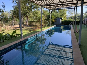 A swimming pool with tiled edges, surrounded by a covered area with metal beams and a grassy lawn. - Morocco blue cafe by chilong river farm  (Kosum Phisai)