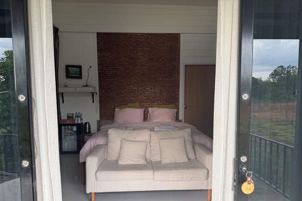 A bedroom with a bed, pillows, a nightstand, a picture frame, and a brick wall.