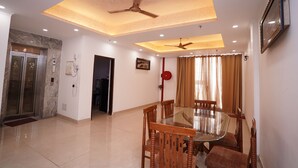 A spacious dining area with a glass table and wooden chairs, ceiling fans, recessed lighting, and a marble wall. - Hotel Lyf Corporate Suites Noida Sec-56 (Noida)