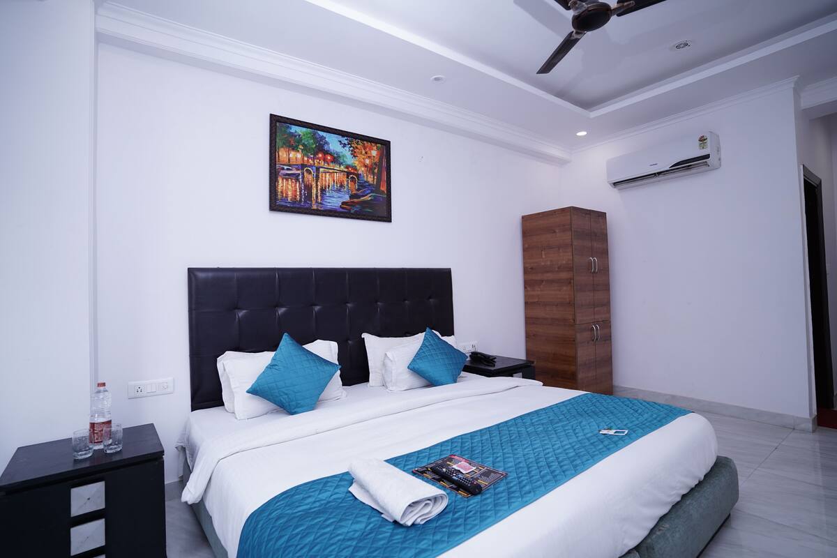 Una habitación de hotel moderna con una cama grande, un cuadro en la pared, un equipo de aire acondicionado y un armario de madera.