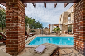 A pool area with a brick wall, lounge chairs, and a hanging chair. - Villa Ivan ZadarVillas (Novigrad)