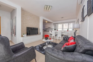 Un salon moderne avec un canapé gris, un téléviseur à écran plat et un coin repas avec des chaises blanches.